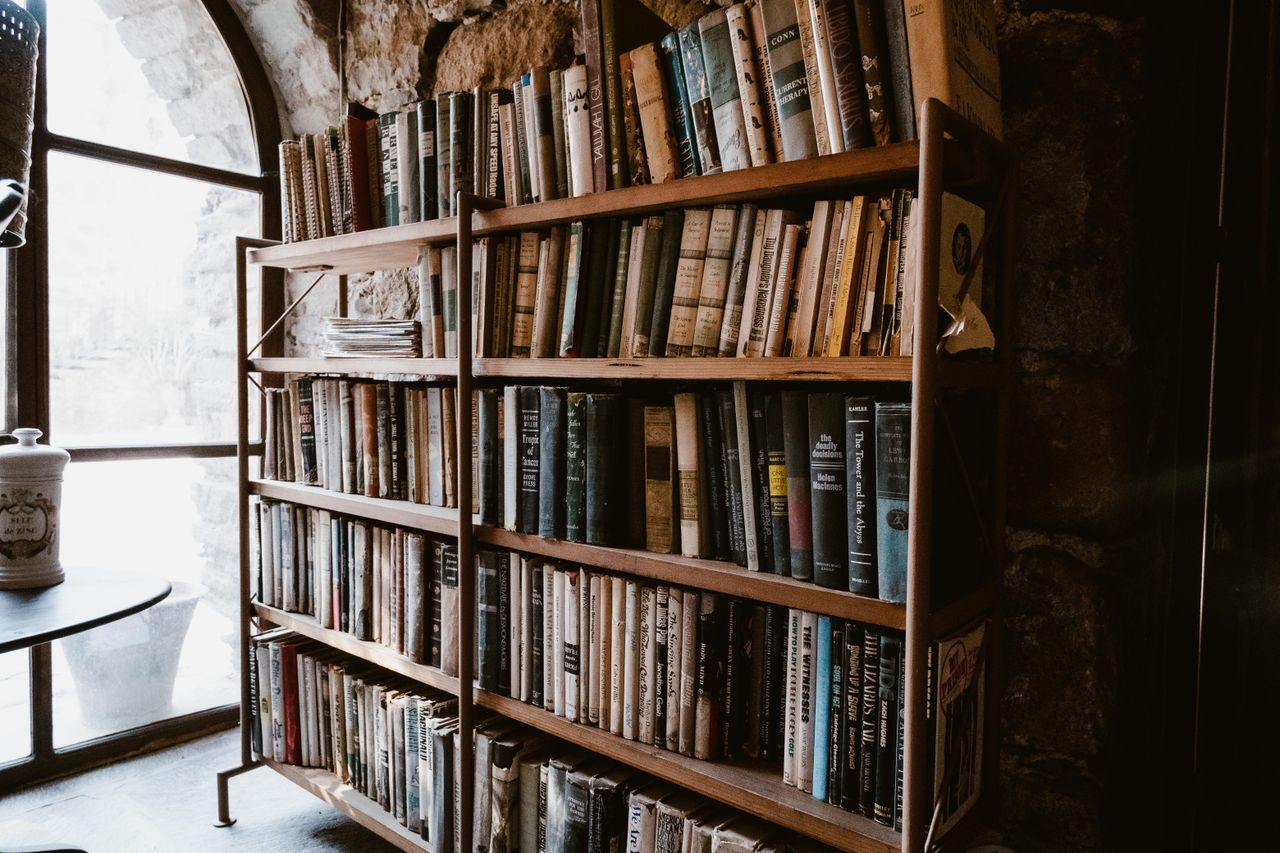 Vintage library setting with wooden bookshelves and natural light through an arched window.
