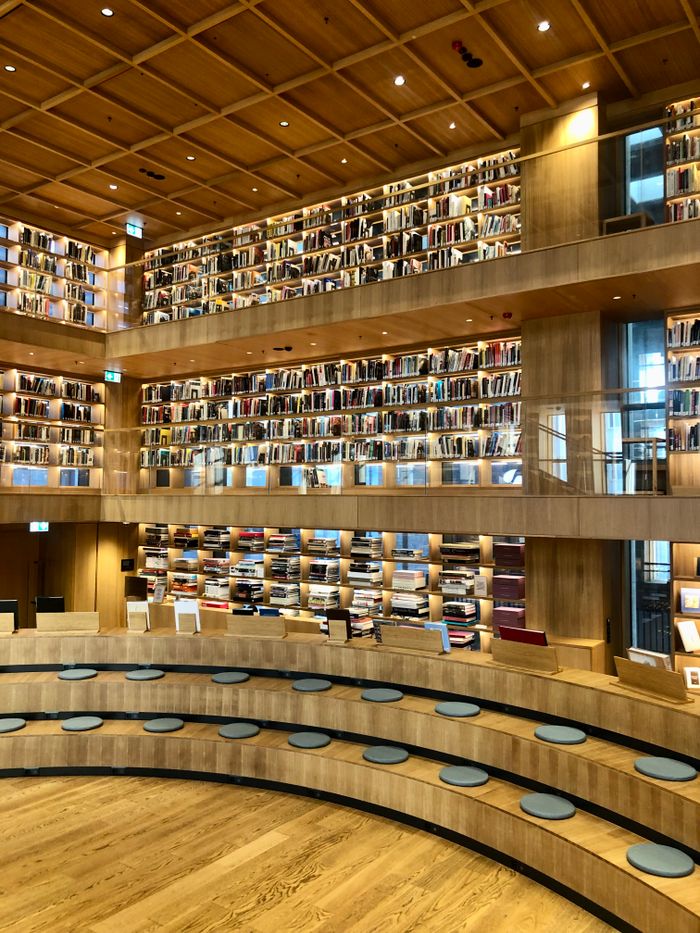 Spacious library interior with circular seating and extensive wooden bookshelves filled with books.